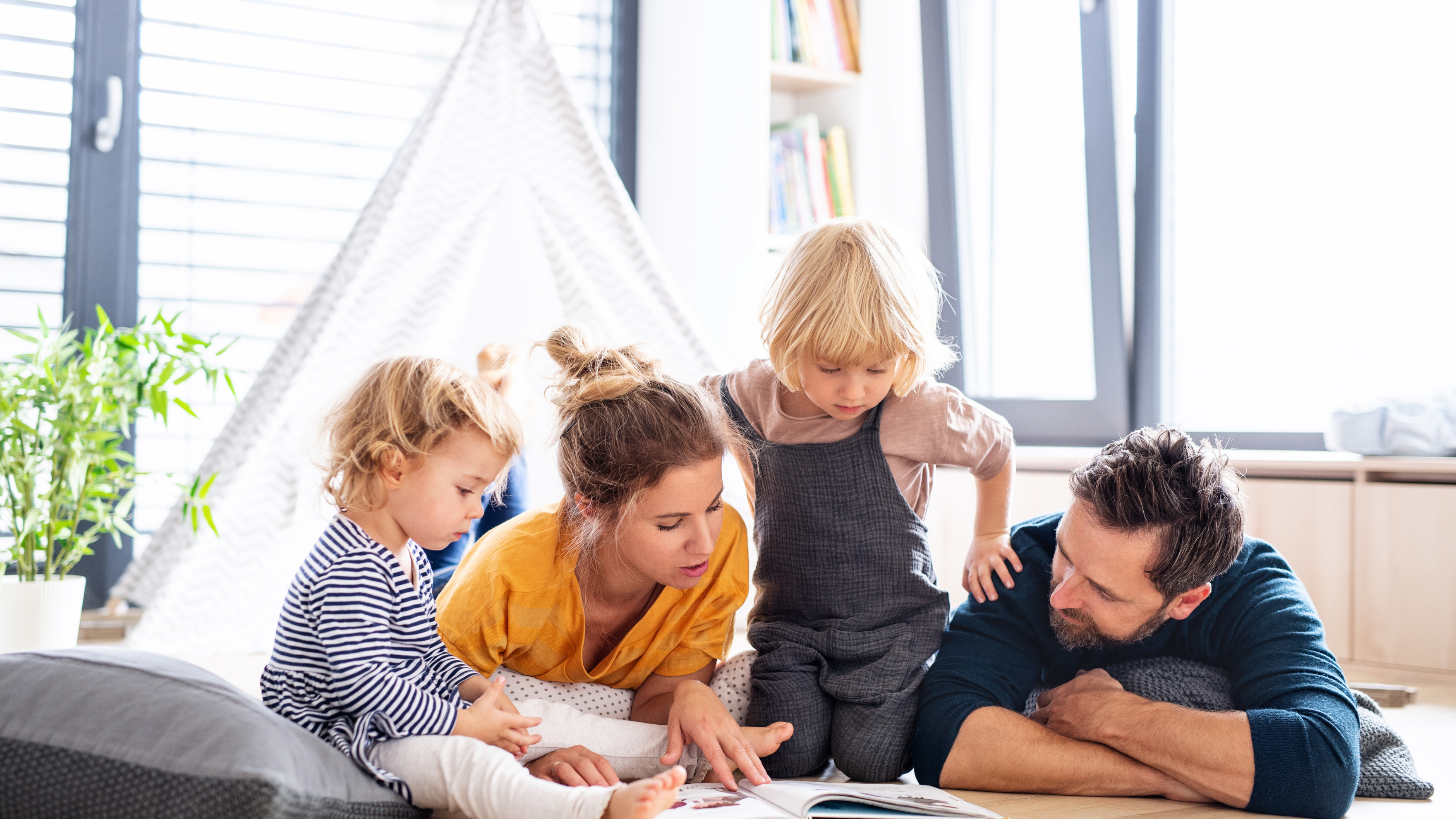 Family of four learning about money together in a cozy living room. Showing that financial literacy for kids doesn’t have to be difficult.