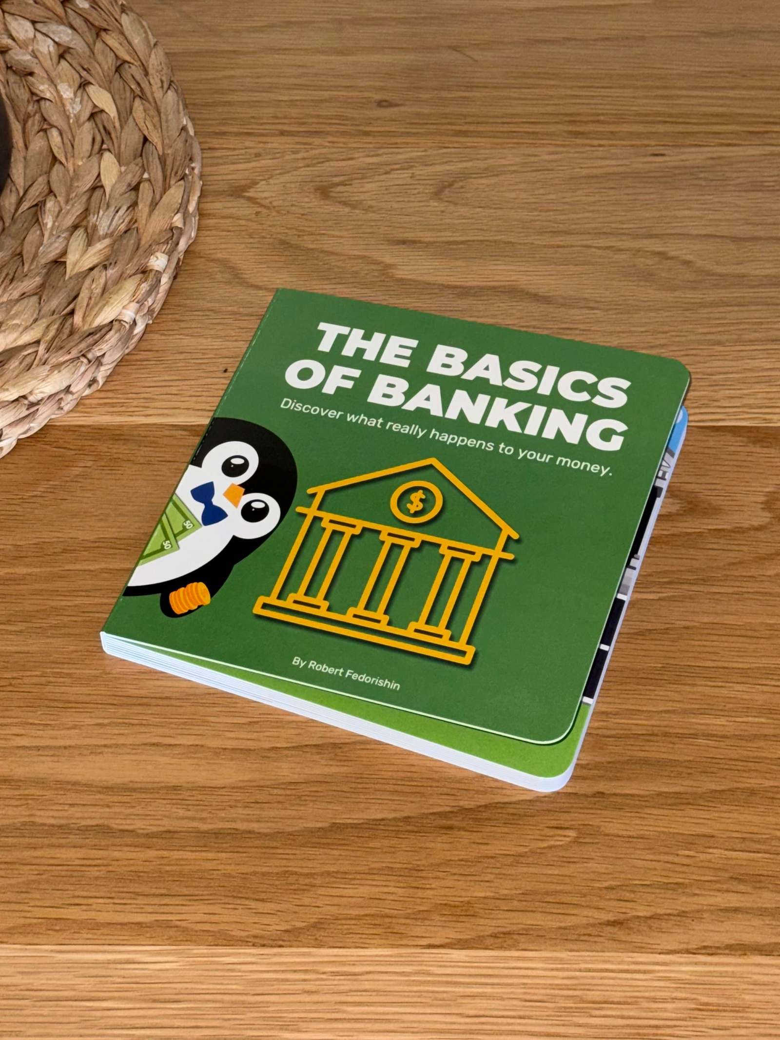 Kid’s money book titled 'The Basics of Banking' with a penguin illustration laid out on a wooden surface.