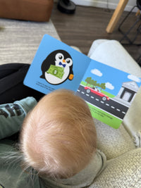 A parent snuggling with their child on a couch reading children’s book about money. 